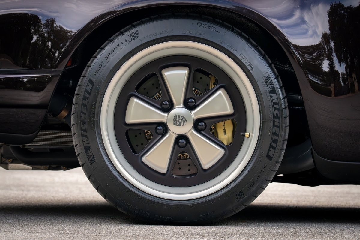 Close-up of an aubergine metallic 1990 Singer Porsche 911 with Fuchs-style wheels and gold brake calipers.