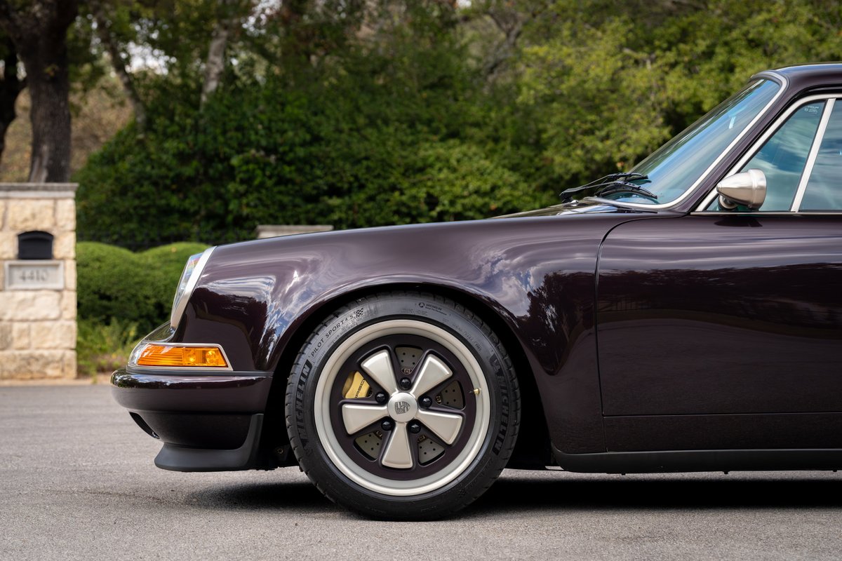 Close up of an aubergine metallic 1990 Singer Porsche 911 with Fuchs wheels and yellow brake calipers.