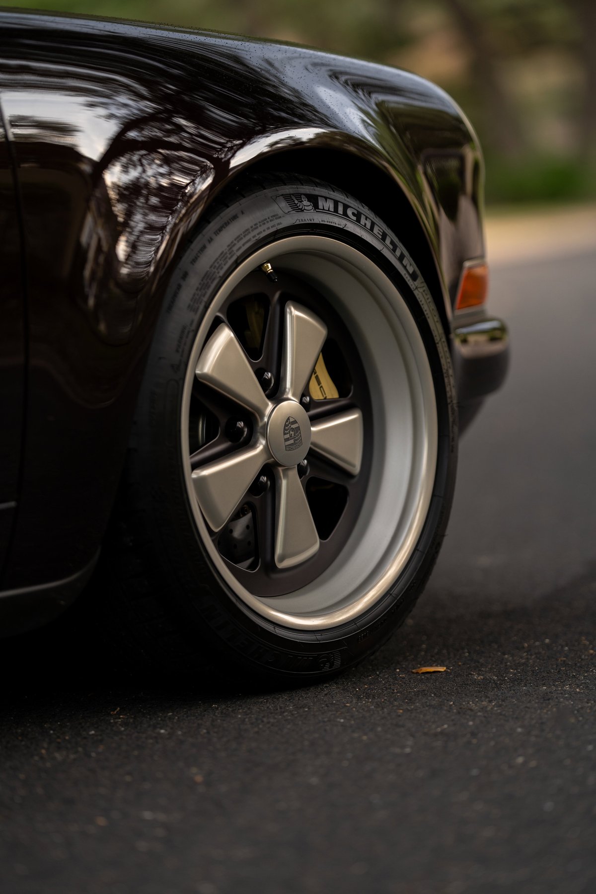 Close-up of an aubergine metallic 1990 Singer Porsche 911 with Fuchs rims and yellow brake calipers.
