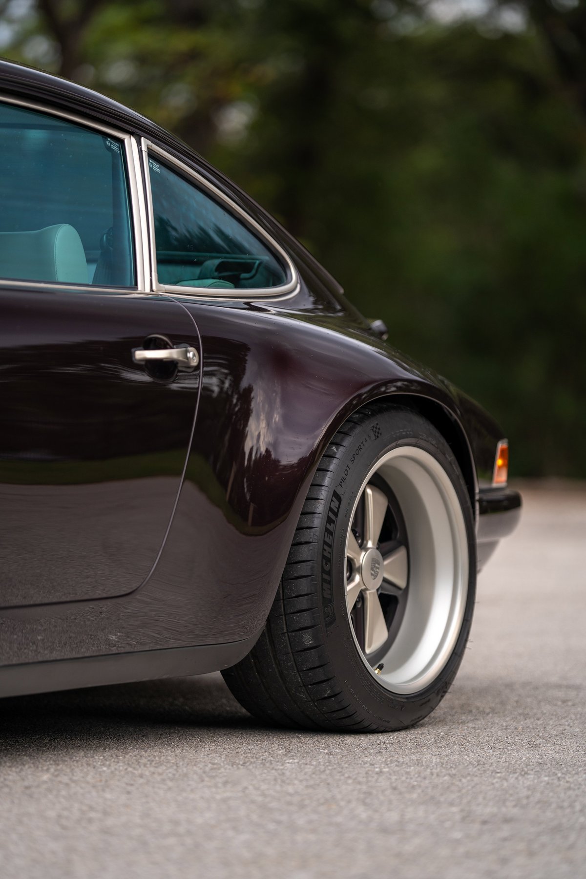 Aubergine Metallic 1990 Singer Porsche 911 rear quarter view showing alloy rims and chrome trim.