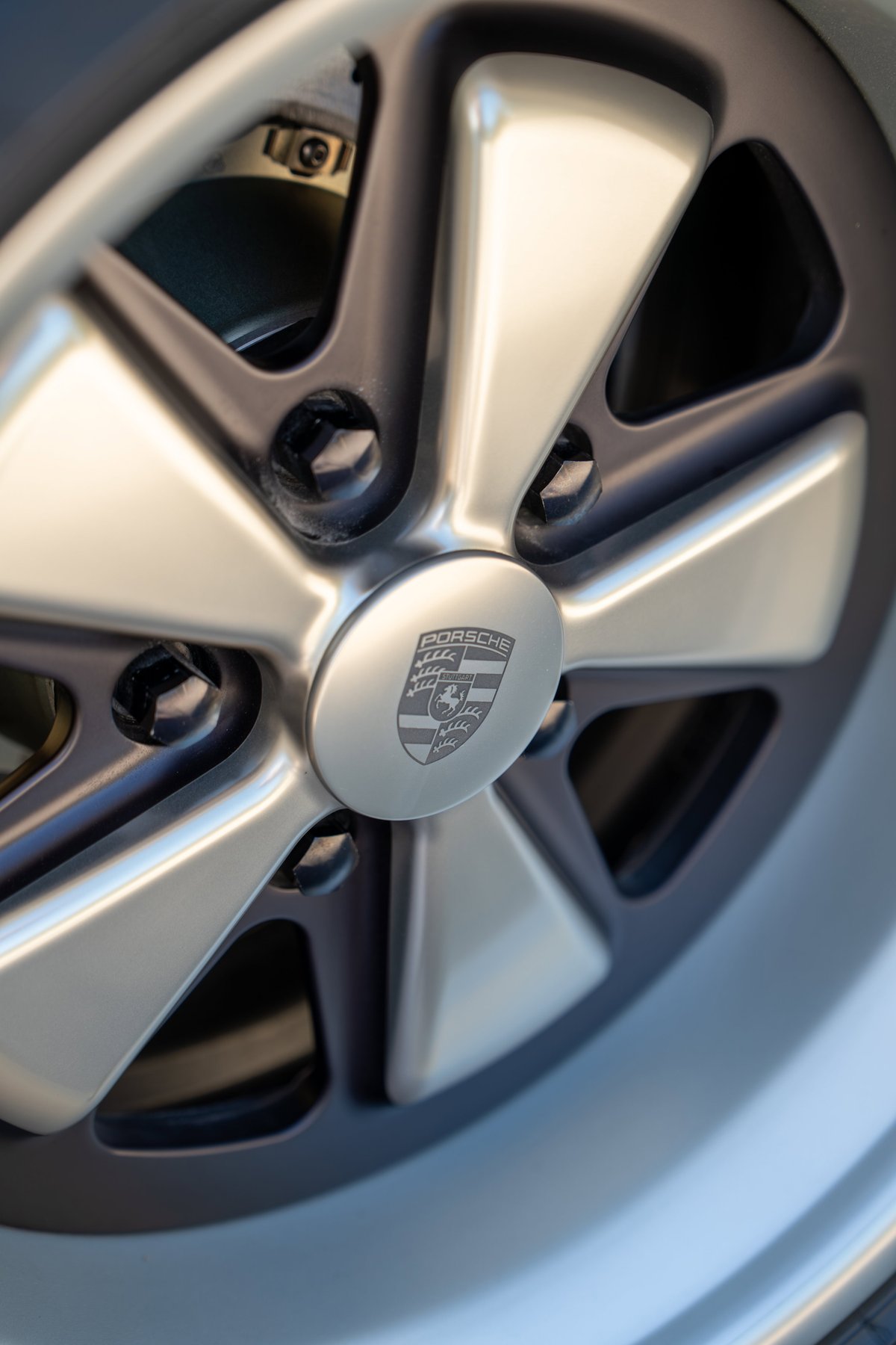 Close-up of a 1990 Porsche 911's brushed metal five-spoke alloy rim with the Porsche crest center cap.