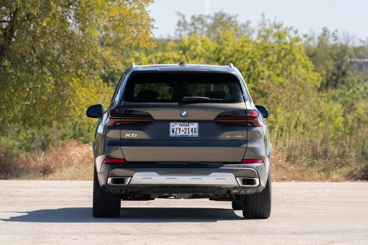 Rear view of a 2026 BMW X5 in Manhattan Green metallic, showing its dual exhaust and silver trim.