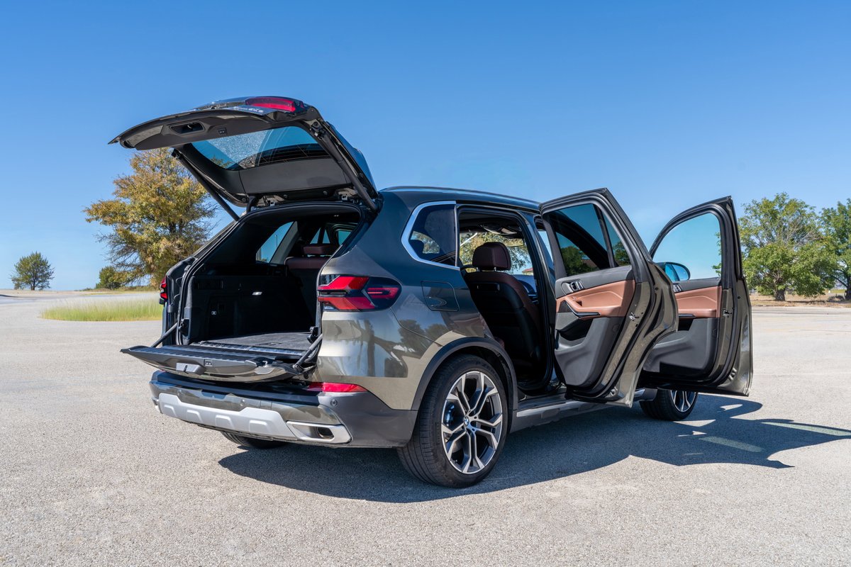 2026 BMW X5 in Manhattan Green with rear hatch and doors open, showing tan leather interior and alloy rims.