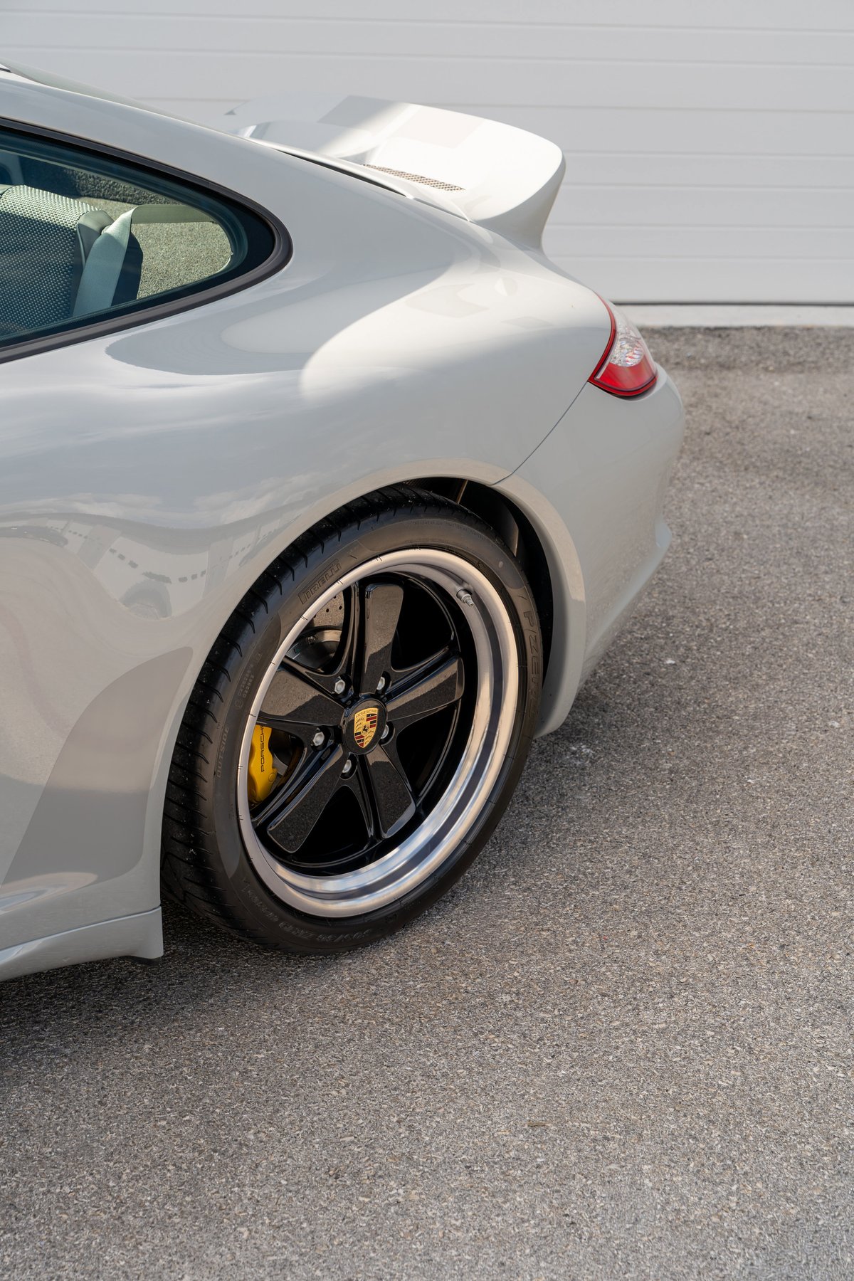 Rear three-quarter view of a grey 2010 Porsche 911 Sport Classic with black five-spoke rims.