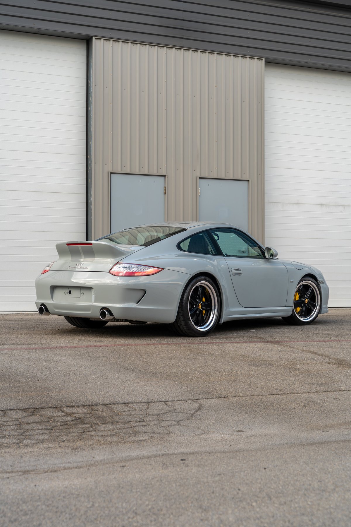 2010 Porsche 911 Sport Classic in Sport Grey, with silver racing stripes and black multi-spoke rims.