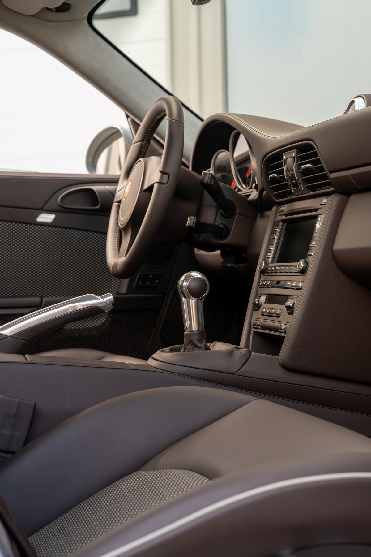 Interior of a 2010 Porsche 911 Sport Classic in brown leather with brushed aluminum trim and a manual shifter.