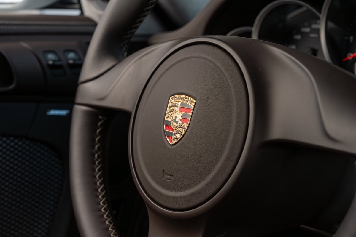 Close up on the dark interior of a 2010 Porsche 911 Sport Classic, showing the steering wheel with the Porsche crest.