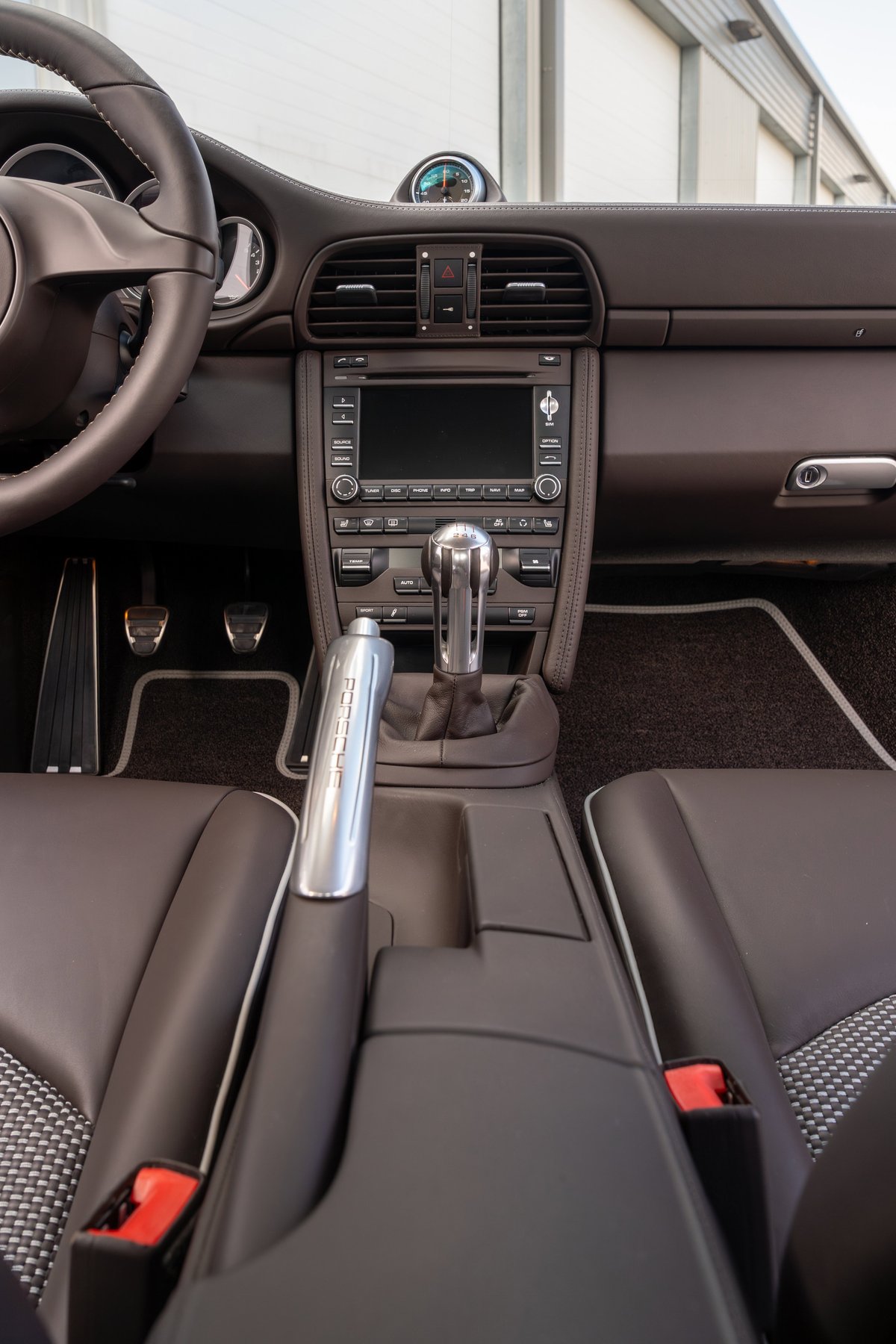 Interior view of a 2010 Porsche 911 Sport Classic in dark brown leather, featuring a manual shifter and SportDesign pedals.