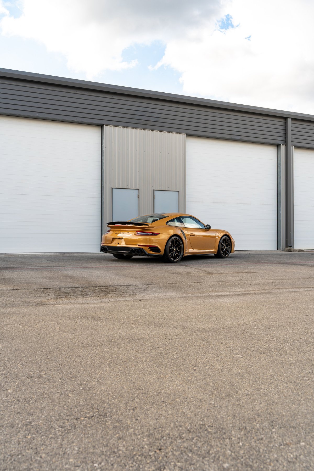 Gold 2018 Porsche 911 Turbo S Exclusive Series with black rims and active spoiler.