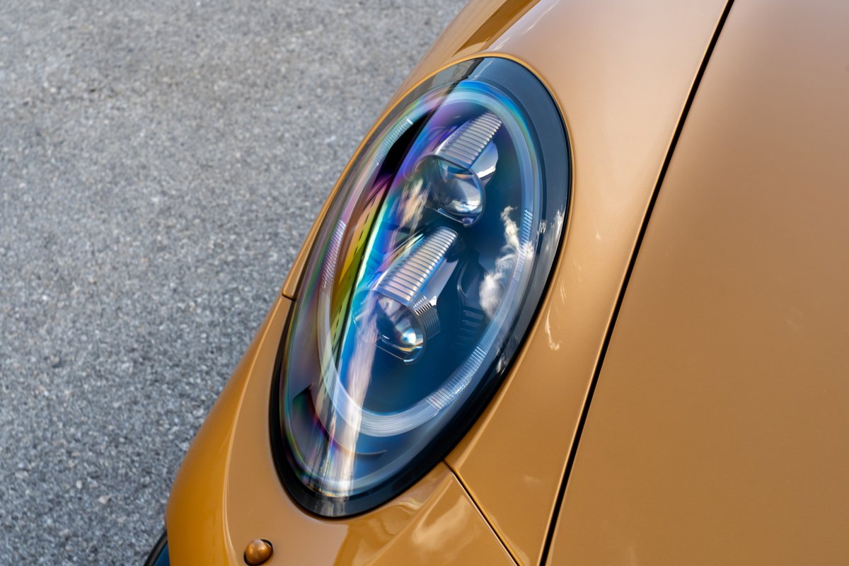 Close-up of a 2018 Porsche 911 Turbo S Exclusive Series headlight in gold metallic paint.