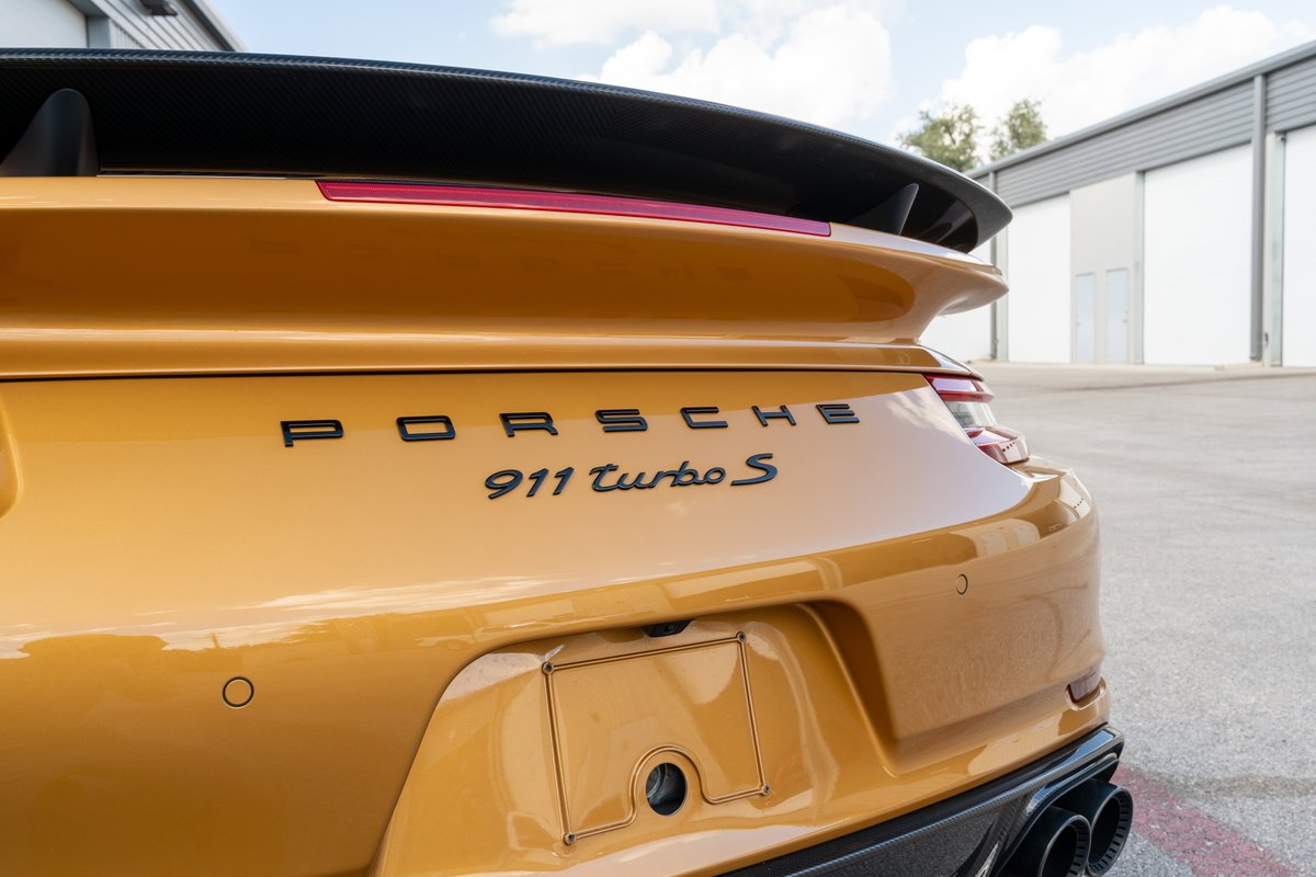 Rear view of a gold 2018 Porsche 911 Turbo S Exclusive Series with black badging and a carbon fiber spoiler.