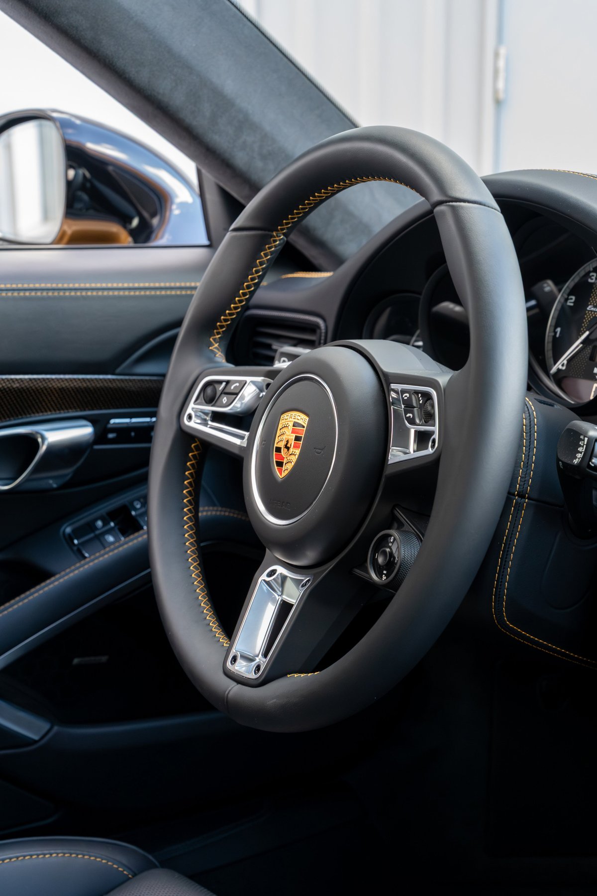 Porsche 911 Turbo S steering wheel with yellow stitching and chrome trim.