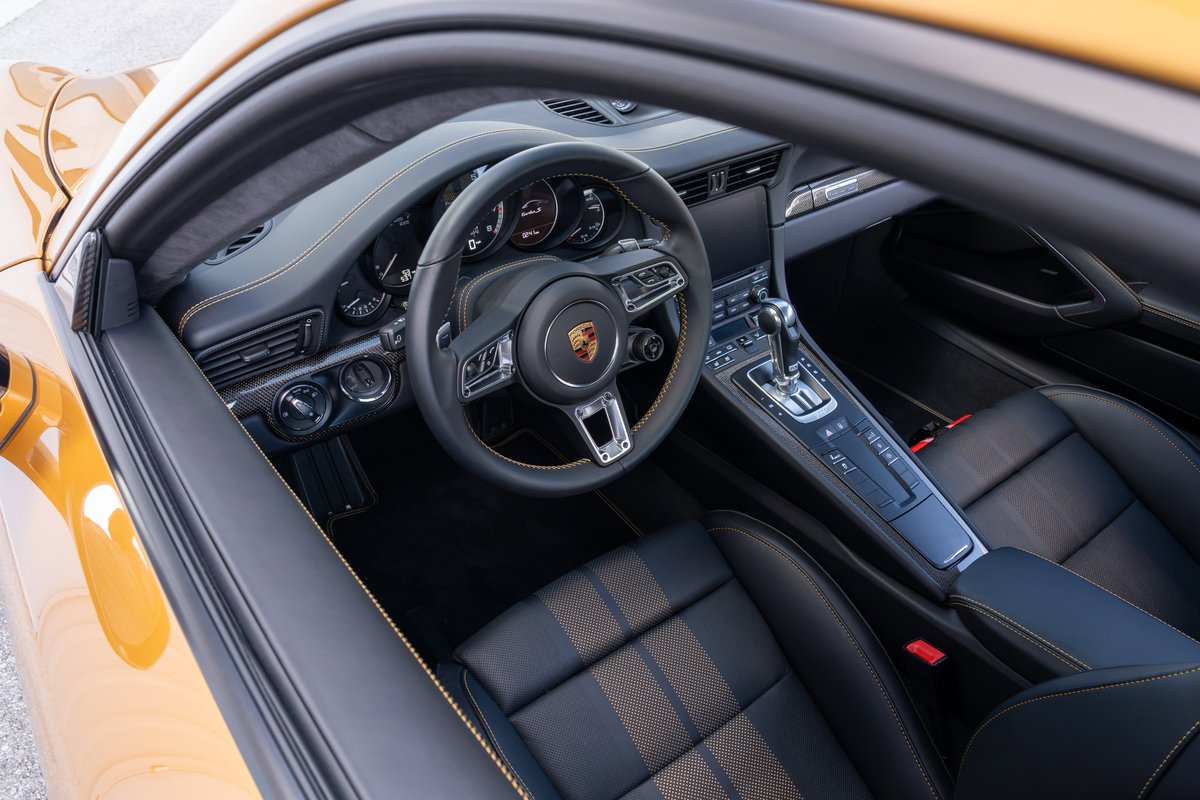 Interior view of a 2018 Porsche 911 Turbo S Exclusive Series in gold, with black leather seats and orange stitching.