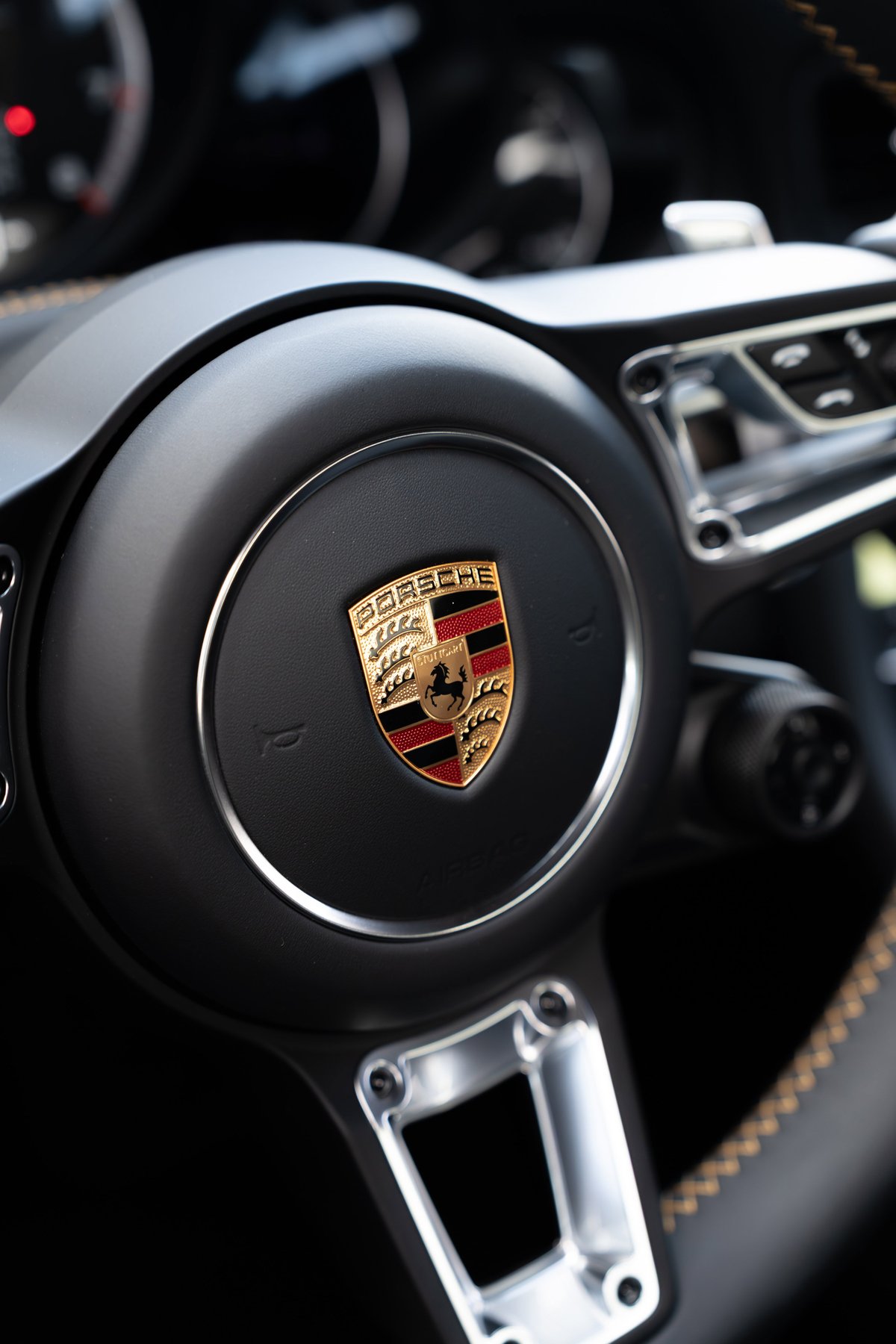 Close-up of a black 2018 Porsche 911 Turbo S Exclusive Series steering wheel with silver trim and Porsche crest.