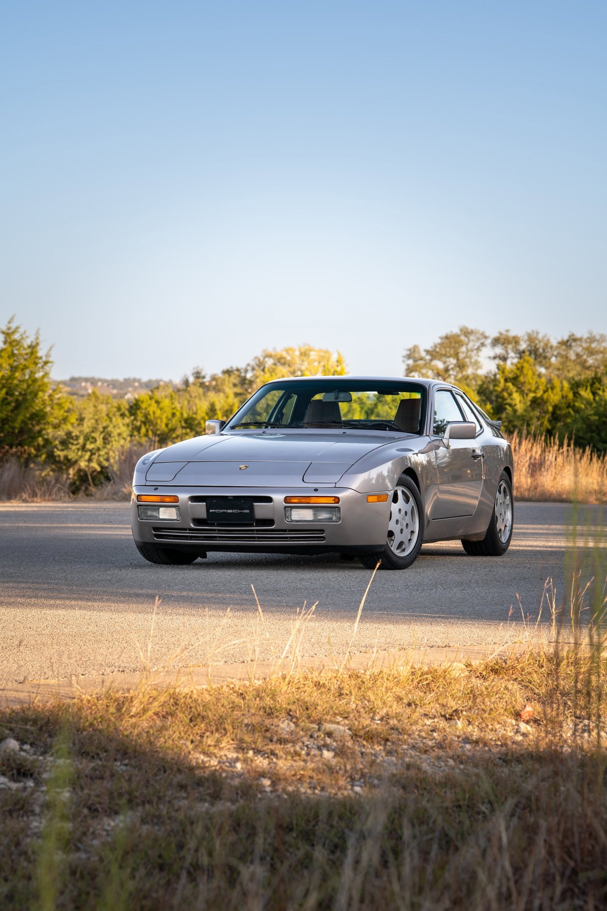 1987 silver Porsche 944 Turbo S coupe with Turbosport rims on a paved road.