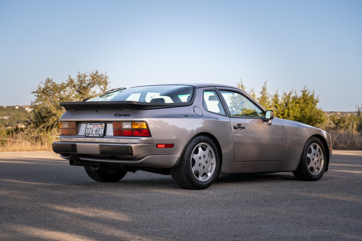 Rear 3/4 view of a silver 1987 Porsche 944 Turbo S with phone dial rims and a rear spoiler.