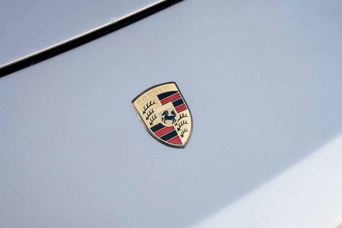Close-up of a vintage Porsche crest emblem on the hood of a silver 1987 Porsche 944 Turbo S.
