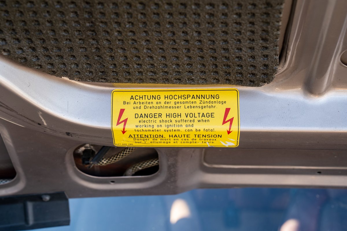 Yellow danger high voltage sticker under the hood of a silver 1987 Porsche 944 Turbo S.