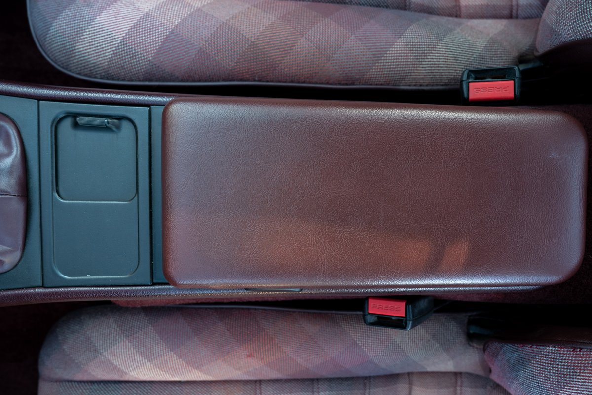 1987 Porsche 944 Turbo S interior: brown leather armrest, plaid seats, and grey trim.