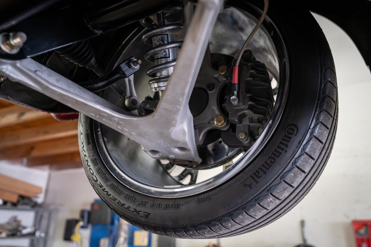 Low angle shot of a 1965 Chevrolet Corvette rear suspension, showing brake caliper, coilover, and Continental tire.