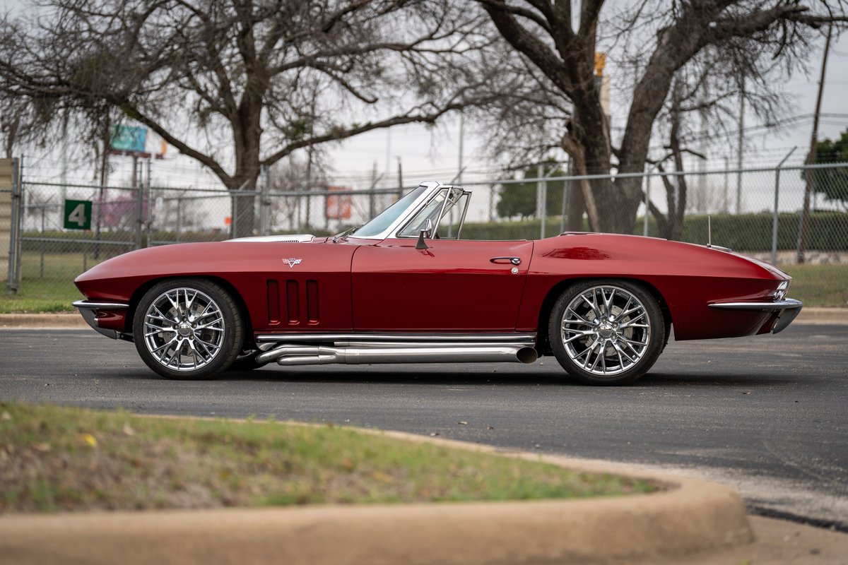 1965 Chevrolet Corvette convertible in red with chrome side pipes and custom chrome rims.