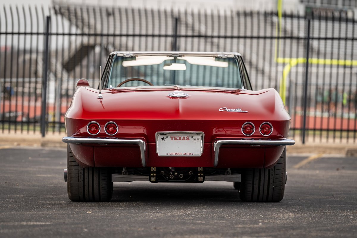 Rear view of a red 1965 Chevrolet Corvette convertible with quad taillights and chrome bumper.