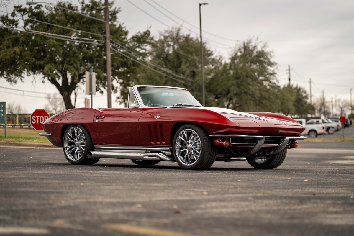 A red 1965 Chevrolet Corvette convertible with chrome side pipes and custom rims.