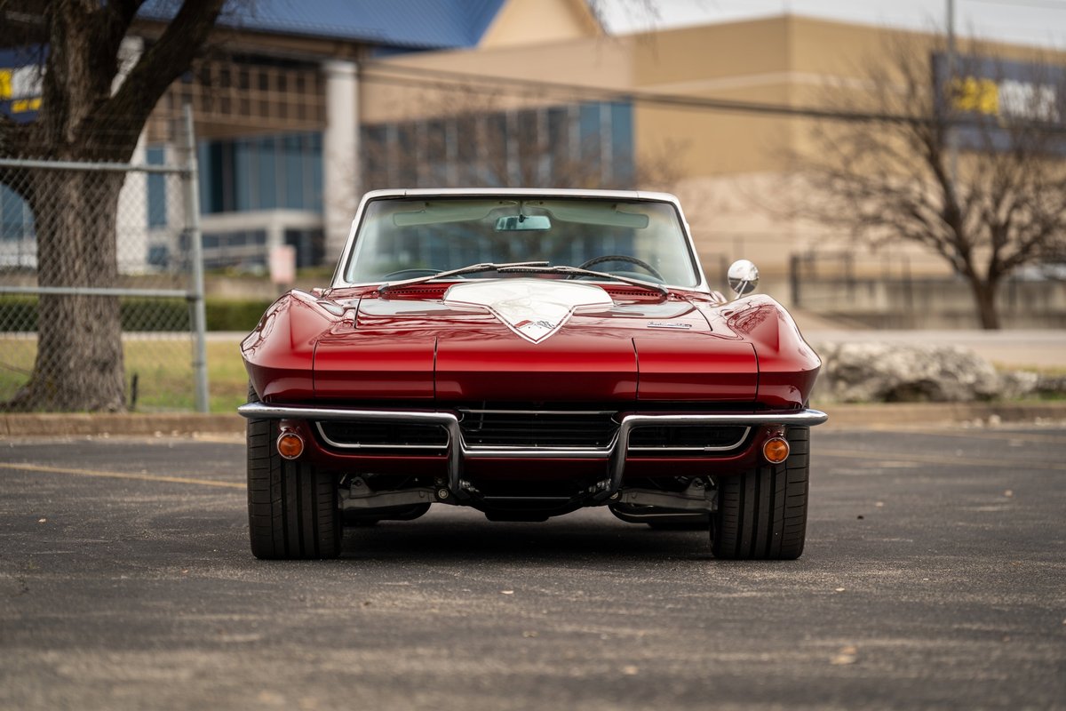 Front view of a red 1965 Chevrolet Corvette Sting Ray with white hood trim and chrome bumpers.