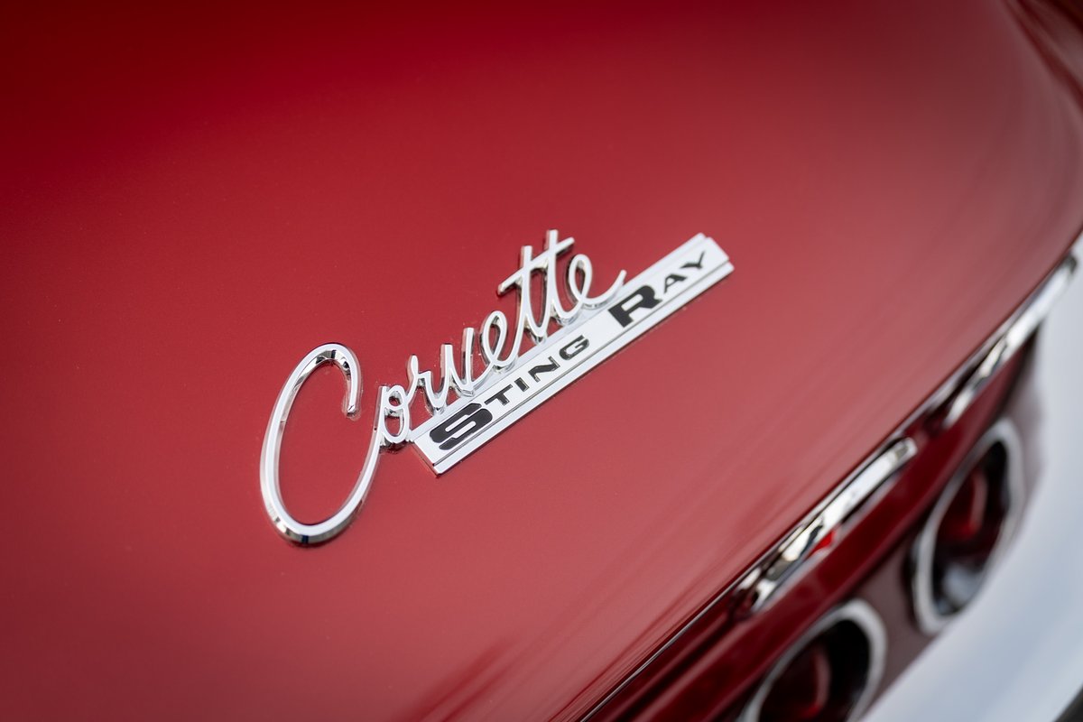 Close-up of red 1965 Corvette Sting Ray emblem on the trunk lid, showcasing chrome trim and taillights.