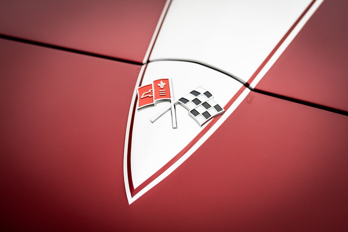 Close-up of red 1965 Corvette hood emblem with flags and checkered flag.