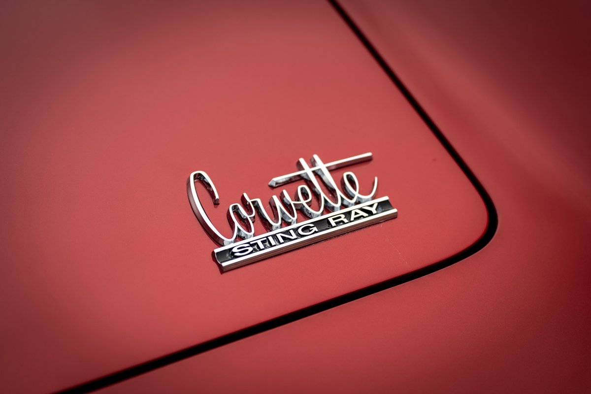 Close-up of a chrome "Corvette Sting Ray" emblem on the red body panel of a 1965 Chevrolet Corvette.