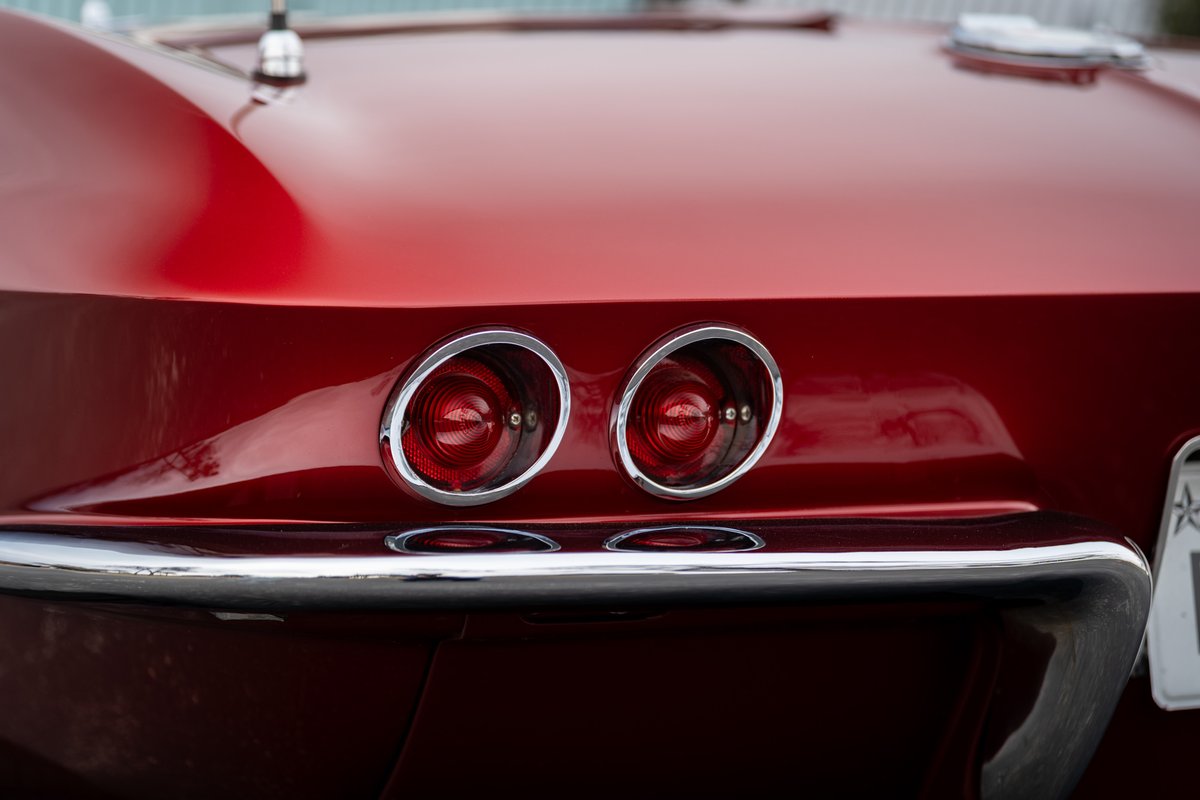 Close up of the iconic dual round taillights and chrome bumper on a red 1965 Chevrolet Corvette.