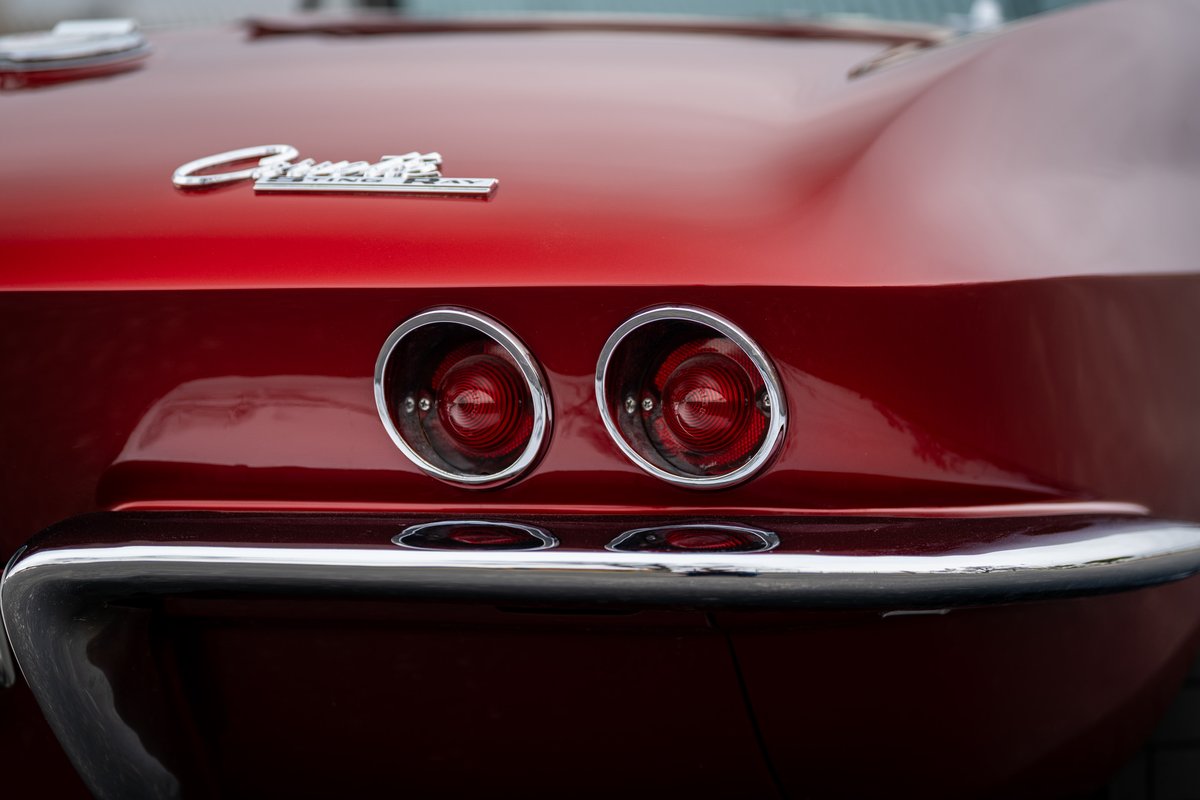 Close-up of the dual taillights and chrome bumper of a red 1965 Chevrolet Corvette.
