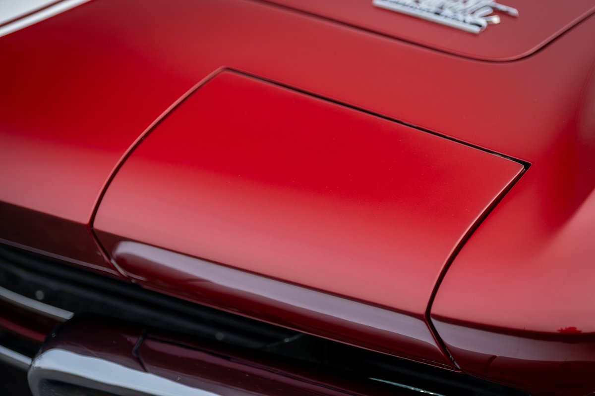 Red 1965 Chevrolet Corvette hood with chrome trim detail.