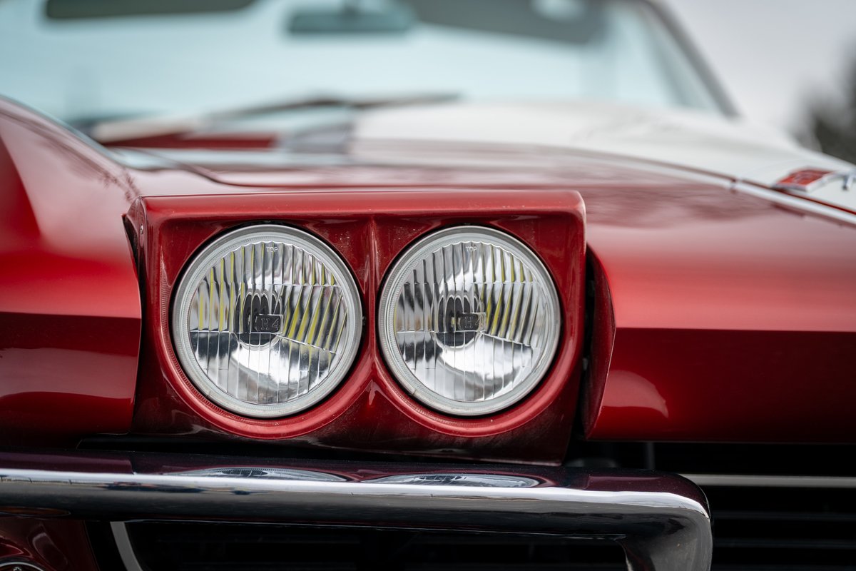 Close-up of a red 1965 Corvette with dual round headlights and chrome bumper.