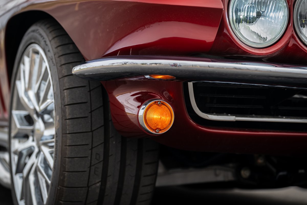 Red 1965 Chevrolet Corvette hot rod, close up of front fender, chrome bumper, and chrome rims.