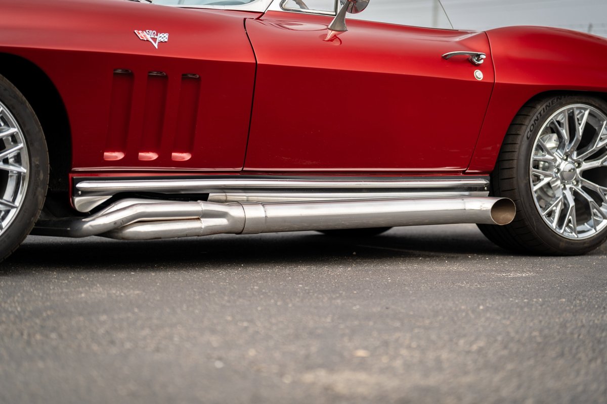 Red 1965 Chevrolet Corvette with side exhaust pipes and chrome rims.