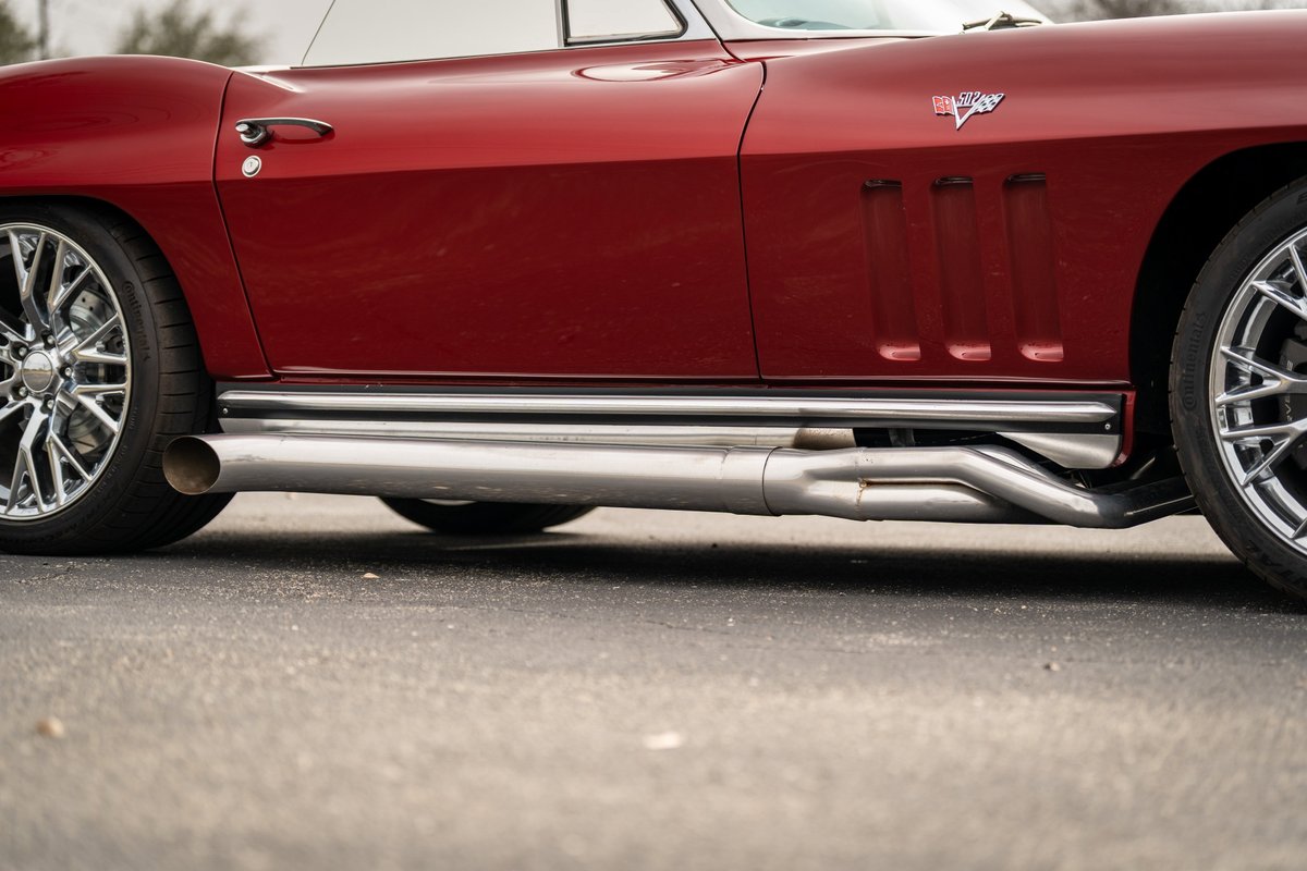 Red 1965 Corvette hot rod with side pipes and chrome rims.