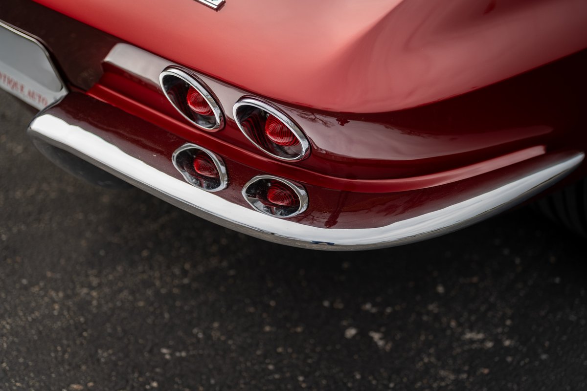 Close-up of a red 1965 Chevrolet Corvette's quad tail lights and chrome bumper trim.