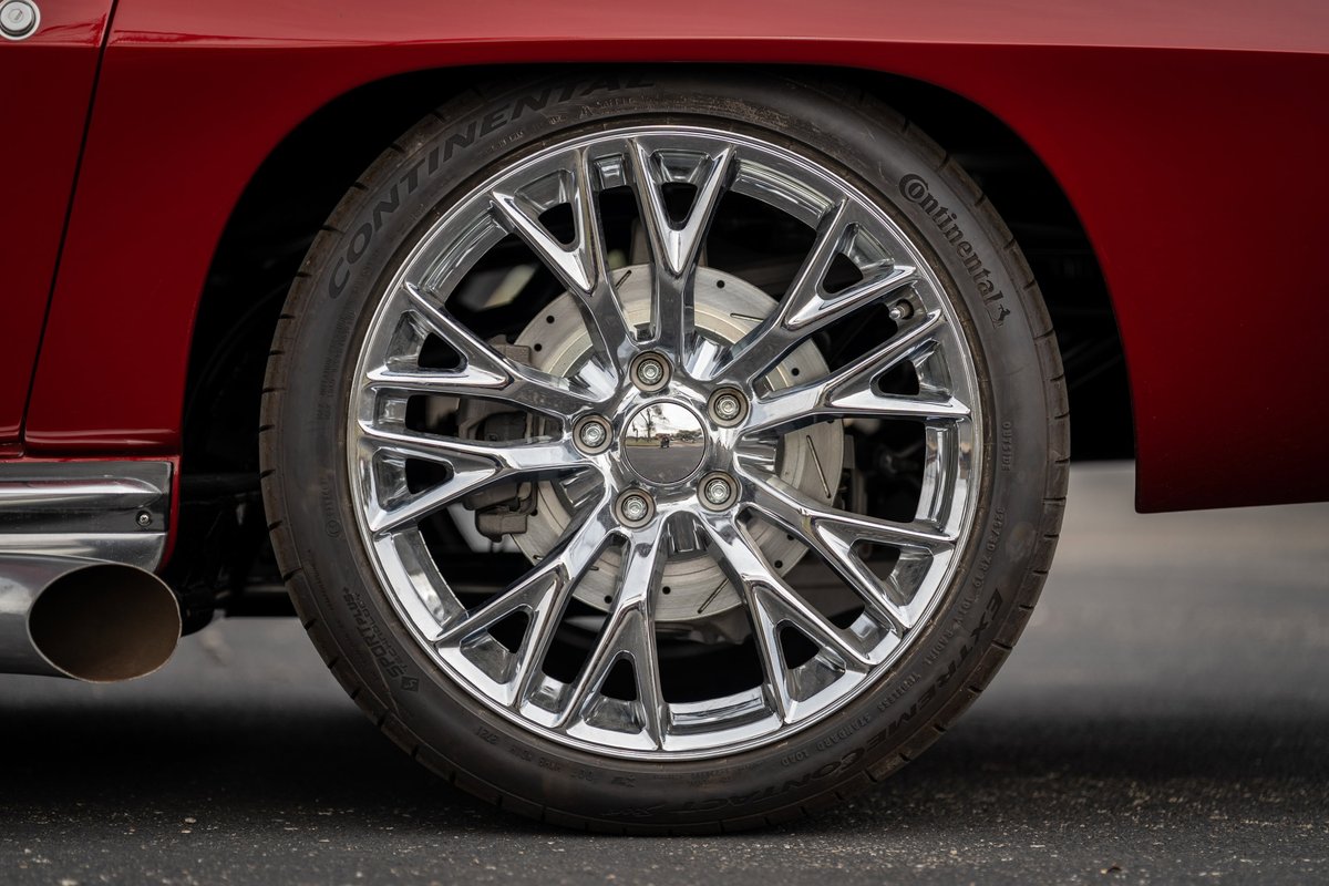 Chrome multi-spoke rims on a red 1965 Chevrolet Corvette with drilled brake rotors.