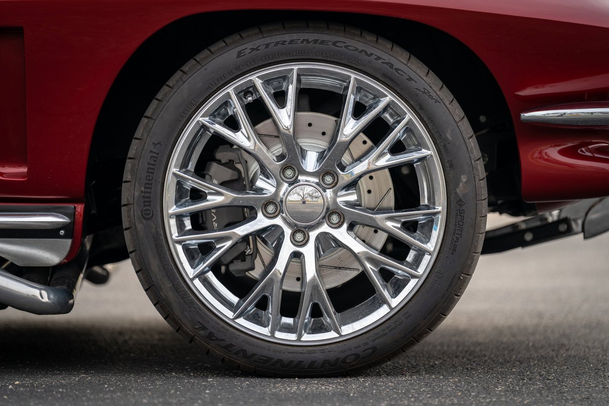 Close-up of a chrome multi-spoke wheel and drilled rotors on a red 1965 Chevrolet Corvette.