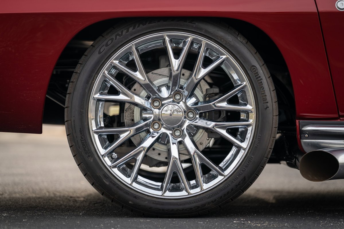 Chrome multi-spoke rims on a red 1965 Chevrolet Corvette Hot Rod with drilled brake rotors.