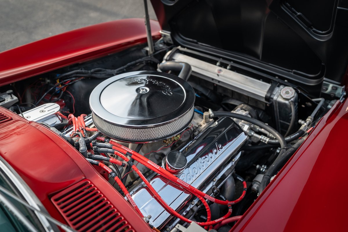 1965 red Corvette engine bay, showcasing chrome valve covers and red spark plug wires.