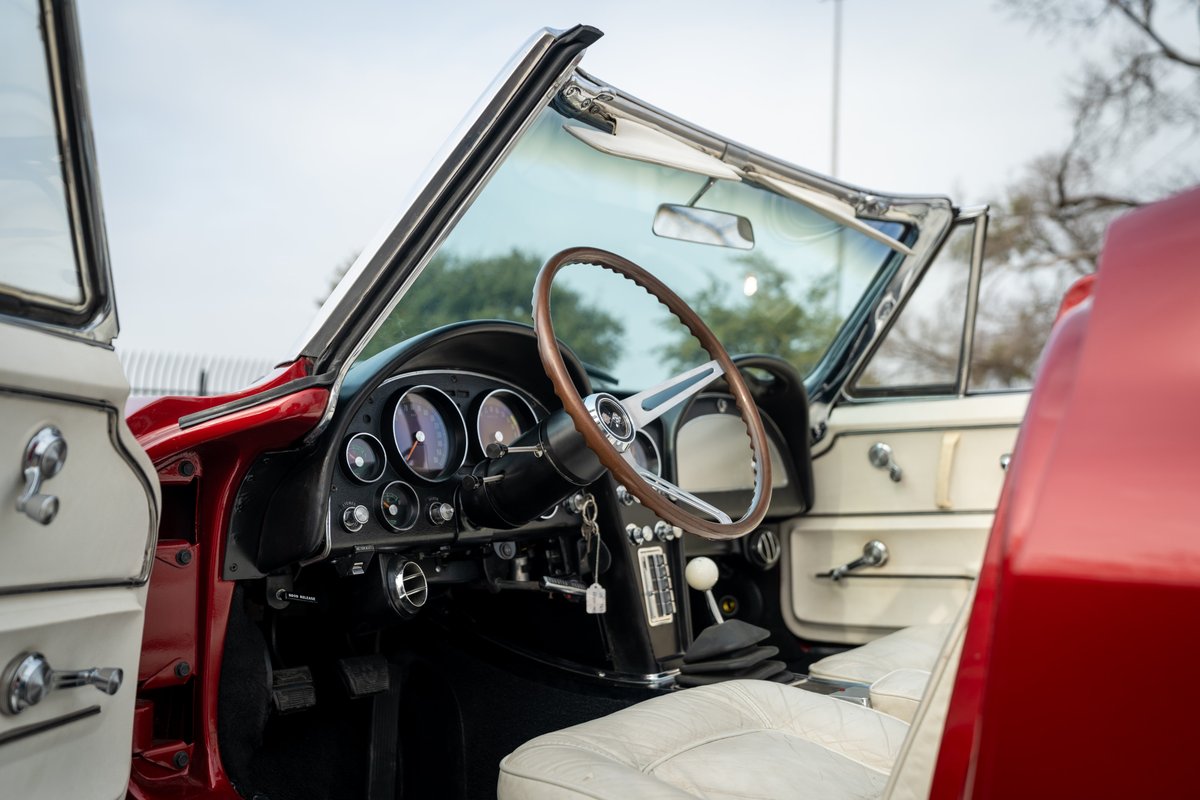 1965 Corvette interior, white seats, wood steering wheel, manual shifter, red exterior trim.