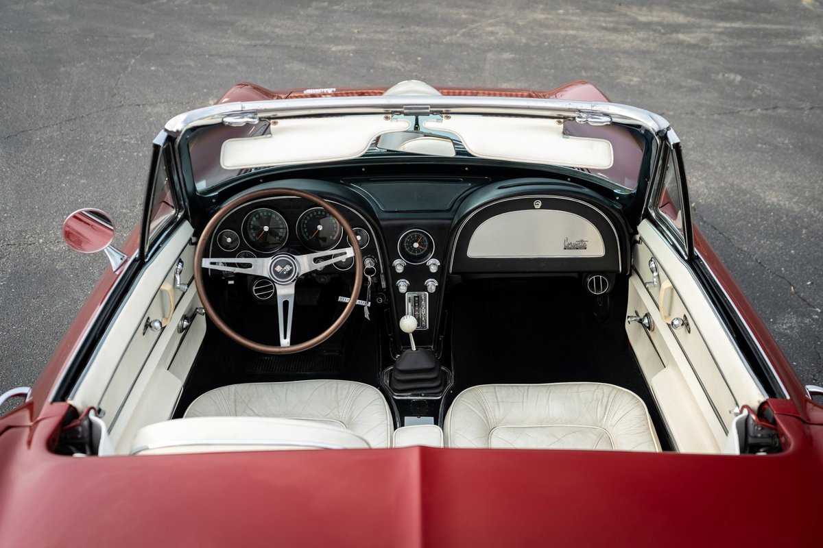 1965 Chevrolet Corvette interior with white seats, wood-rimmed steering wheel, and floor shifter.