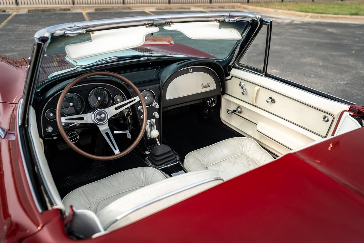 1965 red Corvette convertible interior. White seats, wood steering wheel, black dash, chrome accents.