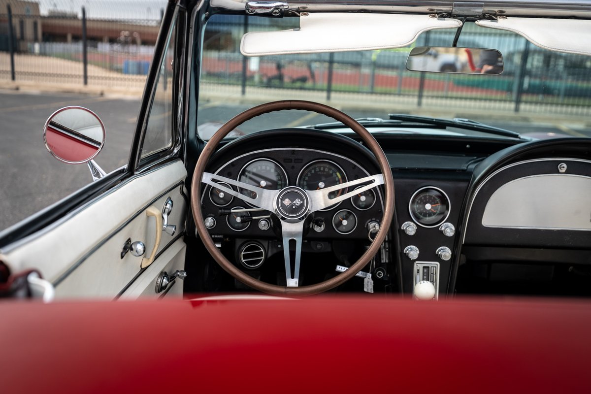 Interior view of a 1965 red Chevrolet Corvette with a classic wood-rimmed steering wheel and dashboard.