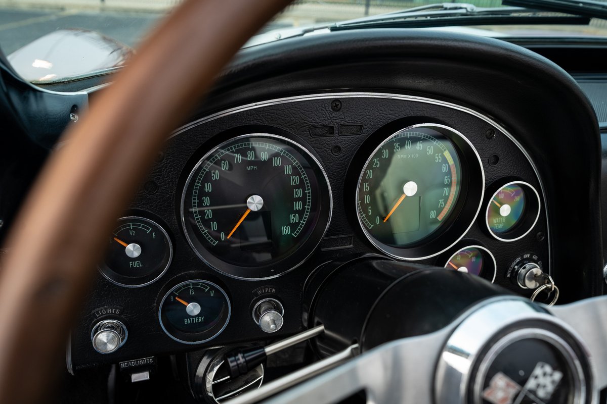 1965 Chevrolet Corvette dashboard with analog gauges and a wooden steering wheel.