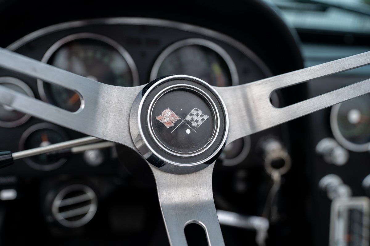 Classic 1965 Corvette steering wheel with iconic crossed flags emblem and brushed metal spokes.