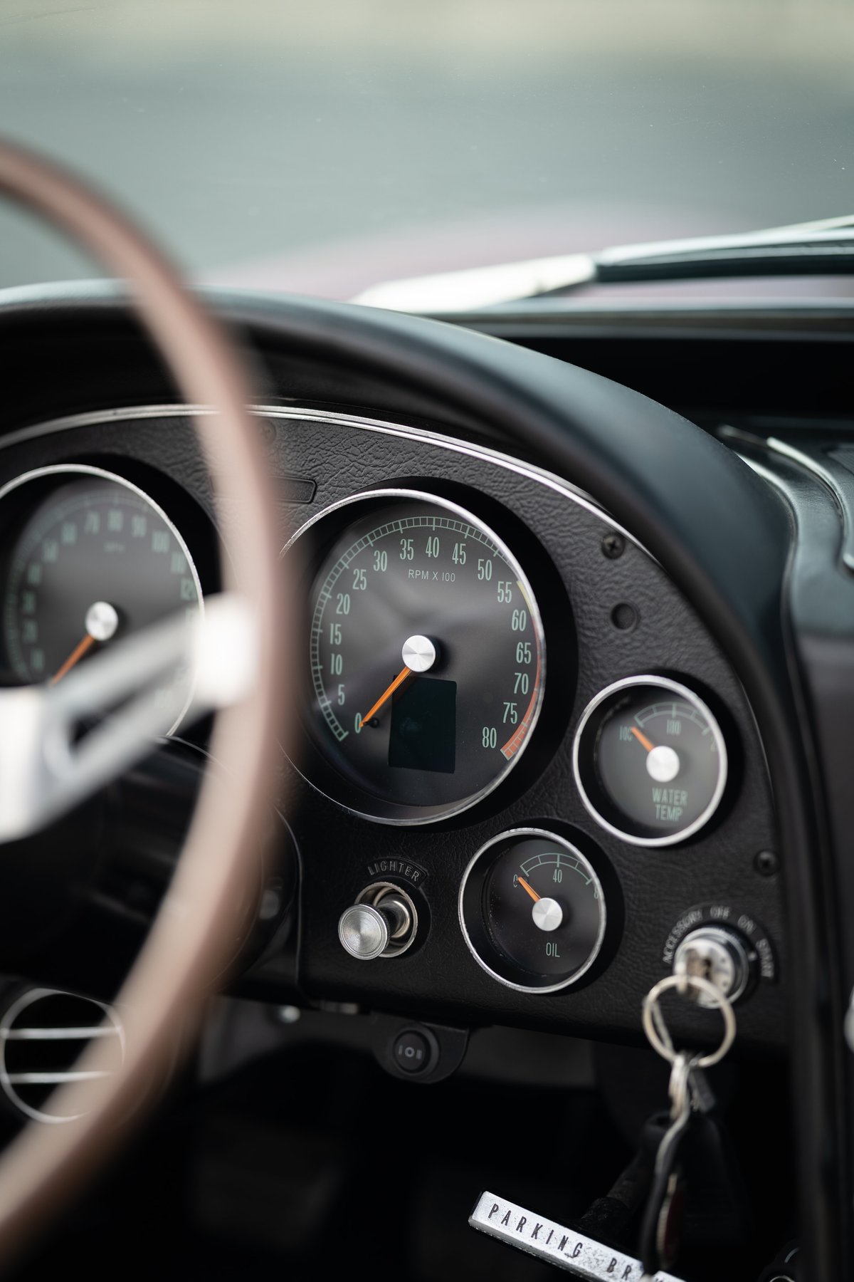 Close-up of a 1965 Chevrolet Corvette's dashboard, featuring classic gauges and a wooden steering wheel.